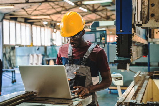 A close-up portrait of an occupational health and safety worker wearing a hard hat and safety glasses looking towards an object.