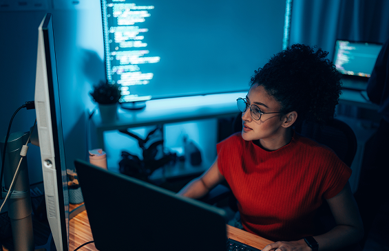 Female Hispanic programmer coding at a multi-monitor workstation, authentic tech workplace and innovation scene