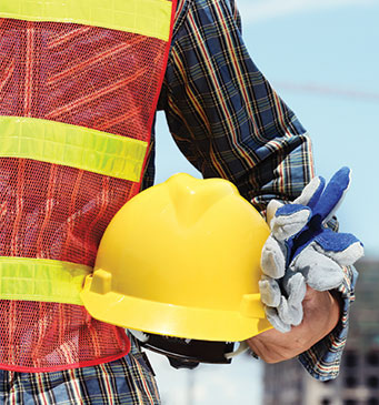 one person with a safety vest on and holding a helmet and gloves in hand