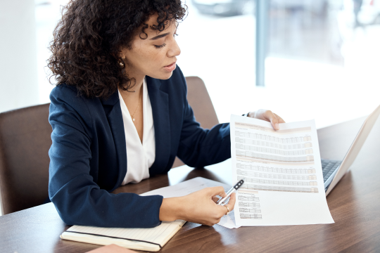 Professional reviewing a printed financial report and pointing to data beside a laptop.